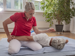 Physiotherapeutin behandelt Patienten auf Bodenmatte mit Dehnungstechnik für die Schulter.